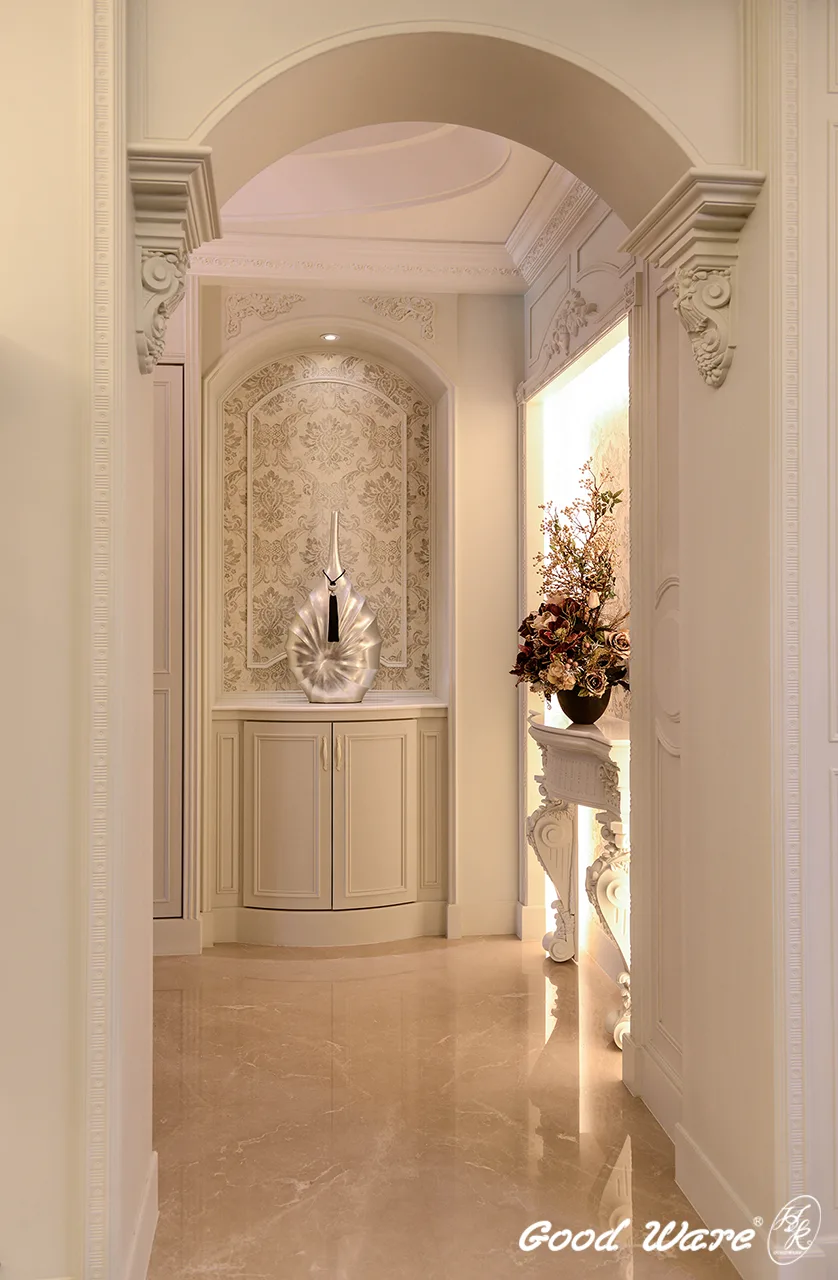 廊道盡頭以門窗框線板修飾，素花色壁紙提升空間典雅、靜謐氛圍，以壁爐柱做置物平台，緊鄰另一側的櫃體則與通往客廳的拱門相呼應。